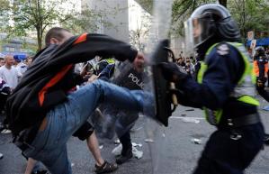 Blue jean's clad thug kicks the shield of the riot police.